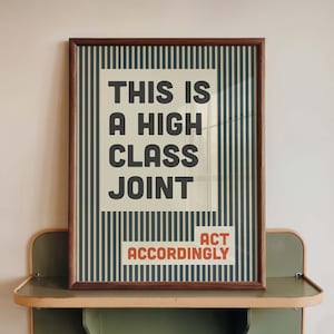 Könnte beinhalten: Ein gerahmter Kunstdruck mit einem vertikalen Nadelstreifenmuster in Dunkelblau und Creme. Der Text lautet THIS IS A HIGH CLASS JOINT in großen dunkelgrauen Buchstaben, mit den Worten ACT ACCORDINGLY in kleineren orangefarbenen Buchstaben unten rechts.