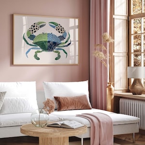 May include: A framed crab art print with a light wood frame. The crab is depicted in shades of green, blue, and black, with a patchwork design. The artwork is displayed in a living room setting with a white sofa and pink curtains.