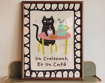 May include: A framed print featuring a black cat sitting at a pink table with a cup of coffee, a croissant, and a light green pitcher. The border has a repeating pattern of white shapes with orange dots. The text reads: Un Croissant, Et Un Café.