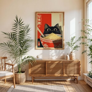 May include: A framed art print featuring a black cat peering over a bowl of noodles. The bowl is red with white floral designs. The background is red and beige with Japanese text. The cat has large, round eyes.