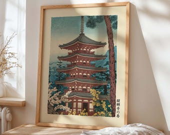 Puede incluir: Impresión enmarcada de una pagoda japonesa con tejado de varios niveles, rodeada de árboles y flores. La obra de arte presenta tonos rojos, azules y verdes, con texto japonés en la esquina inferior derecha. El marco es de madera.