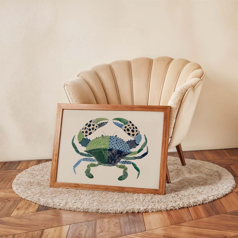 May include: A framed art print featuring a stylized crab illustration. The crab is depicted in shades of green and blue with black and white spotted claws. The artwork is displayed on a cream-colored background within a wooden frame.