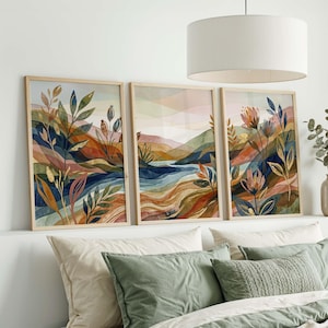 Könnte beinhalten: Drei gerahmte Aquarelldrucke mit Landschaftsmotiven. Jeder Druck zeigt eine Naturszene mit farbenfrohem Laub, Blumen und einem Fluss. Das Kunstwerk ist in Blau-, Orange- und Grüntönen gehalten und hat einen hellen Holzrahmen.