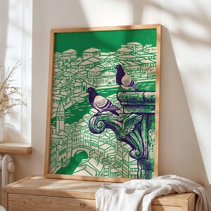 May include: A framed art print featuring a green and white illustration of a cityscape with two pigeons perched on a decorative stone element. The artwork has a vintage aesthetic, with a wooden frame.