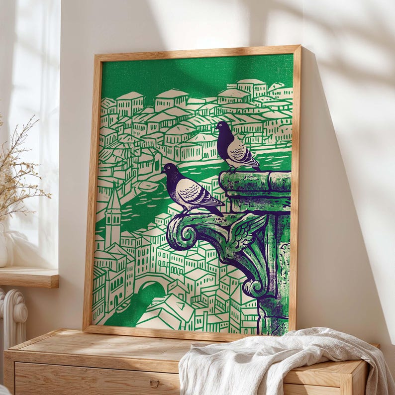 May include: A framed art print featuring a green and white illustration of a cityscape with two pigeons perched on a decorative stone element. The artwork has a vintage aesthetic, with a wooden frame.