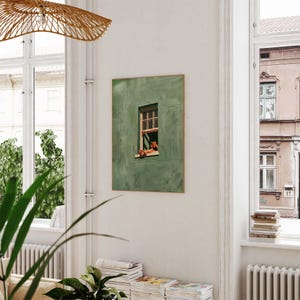 May include: A framed art print featuring a green wall with a window. The window reveals a glimpse of a person relaxing. The artwork is displayed in a bright, airy room with large windows and a woven light fixture.
