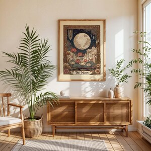 May include: A framed art print depicting a full moon in a night sky, with floral and plant motifs. The artwork has a vintage aesthetic, with a beige border and the words "THE MOON" at the base. The print is displayed above a wooden cabinet.