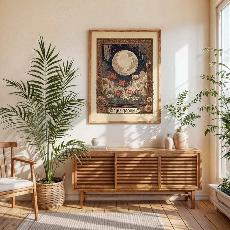 May include: A framed art print depicting a full moon in a night sky, with floral and plant motifs. The artwork has a vintage aesthetic, with a beige border and the words "THE MOON" at the base. The print is displayed above a wooden cabinet.