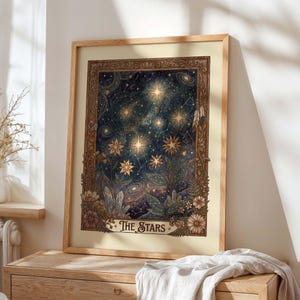 May include: A framed print with the text "The Stars." The artwork depicts a dark blue night sky with shining stars, constellations, and botanical details in green, brown, and beige. The frame is light brown. The print is a decorative item.