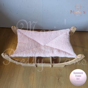 May include: A pale pink pet hammock with a soft, fluffy texture, set within a wooden frame. The frame has a curved, rocking design. The image includes the text "Marie's Pretty Paws" and a note stating "Hammock Frame Not Included."