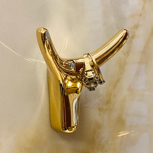 May include: A gold bull head wall hook with a decorative design. The hook is mounted on a white wall.