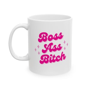May include: White ceramic mug with a pink design that says "Boss Ass Bitch" in a retro font.