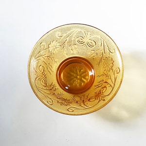 Op de afbeelding: Een vintage amber glazen kom met een bloemenmotief. De kom heeft een reliëf, getextureerd patroon en een gegolfde rand.
