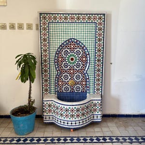 Peut inclure: Une fontaine décorative en mosaïque avec un bassin bleu et des motifs géométriques complexes dans des tons de bleu, vert, rouge et blanc.