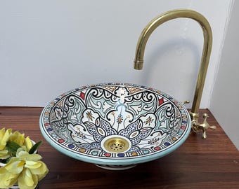May include: A white ceramic sink with a blue and green floral pattern. The sink has a brass faucet with a curved spout.