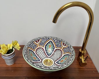 May include: A white ceramic sink with a blue, green, and orange geometric pattern. The sink has a gold drain and is paired with a gold faucet.