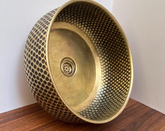 May include: A gold-toned, round, ceramic sink with a textured, honeycomb-like pattern. The sink has a single drain hole in the center.