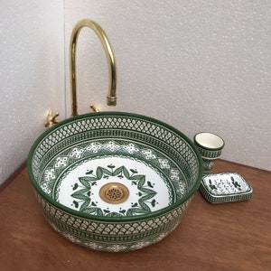 May include: A white ceramic sink with a green and white geometric pattern. The sink is round and has a brass faucet. There is a small green and white soap dish and a green and white cup next to the sink.