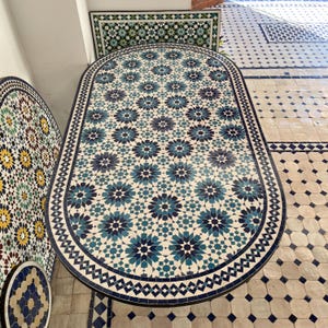 Peut inclure: Plateau de table ovale avec un motif de mosaïque géométrique bleu, blanc et noir. Le plateau de table est fait de carreaux de céramique et a un fond blanc avec un motif répétitif d'étoiles bleues et noires.