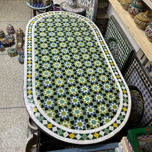 Peut inclure: Plateau de table ovale avec un fond blanc et un motif géométrique de carreaux verts, bleus et jaunes. Le plateau de table est entouré d'une bordure blanche avec un motif géométrique de carreaux verts, bleus et jaunes.