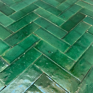 Puede incluir: Primer plano de un suelo de baldosas verdes con un patrón de espiga. Las baldosas son brillantes y reflejan la luz.