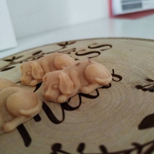 May include: Three small, beige, ceramic dog figurines on a wooden surface with a floral design. The figurines are in a sleeping position.