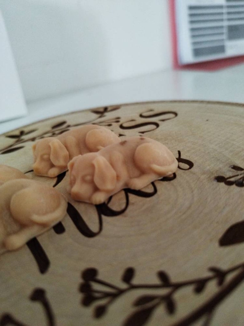 May include: Three small, beige, ceramic dog figurines on a wooden surface with a floral design. The figurines are in a sleeping position.