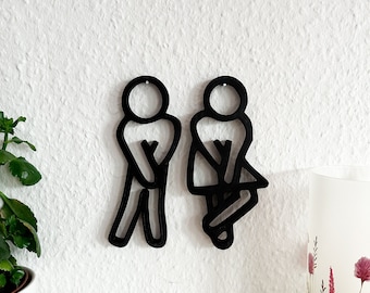 Könnte beinhalten: Schwarze Silhouette Wanddekoration eines Mannes und einer Frau im Badezimmer-Stil. Die Silhouetten sind aus schwarzem Material ausgeschnitten und an einer weißen Wand montiert.