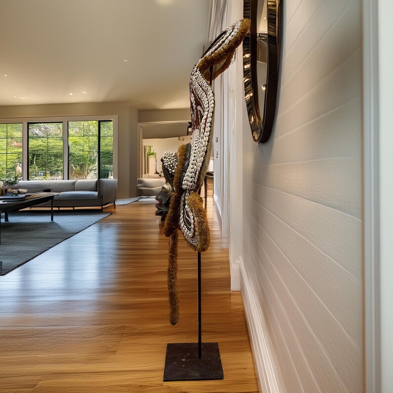 May include: A white and brown decorative sculpture with a long, flowing tail made of natural materials. The sculpture is mounted on a black metal stand and is displayed in a hallway with white walls and wood floors.