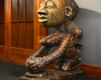 May include: A wooden sculpture of a woman holding a child. The sculpture is painted in gold and brown with white dots. The woman is kneeling and holding the child in her arms. The sculpture is on a wooden base.