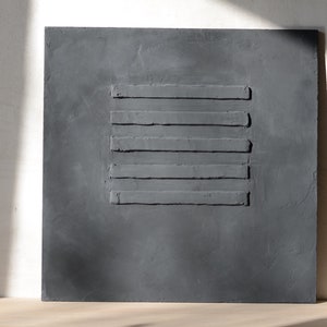 Puede incluir: Una pieza de arte de pared cuadrada de color gris oscuro con cinco l&iacute;neas horizontales en relieve.