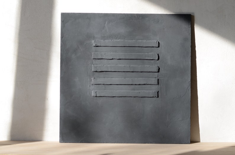 Puede incluir: Una pieza de arte de pared cuadrada de color gris oscuro con cinco l&iacute;neas horizontales en relieve.