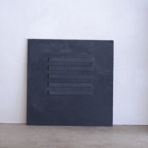Puede incluir: Un lienzo cuadrado gris oscuro con cinco l&iacute;neas horizontales de pintura en relieve en el centro.
