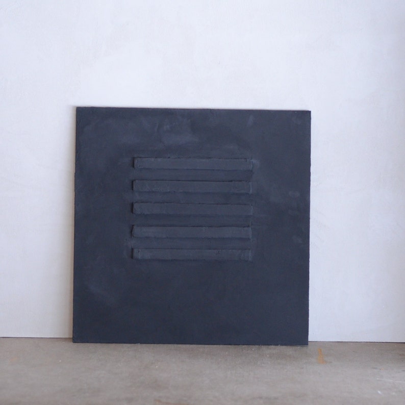 Puede incluir: Un lienzo cuadrado gris oscuro con cinco l&iacute;neas horizontales de pintura en relieve en el centro.