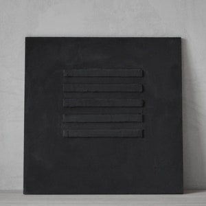 Puede incluir: Un lienzo cuadrado negro con cinco l&iacute;neas horizontales de pintura negra en relieve.