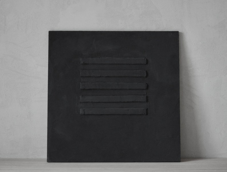Puede incluir: Un lienzo cuadrado negro con cinco l&iacute;neas horizontales de pintura negra en relieve.