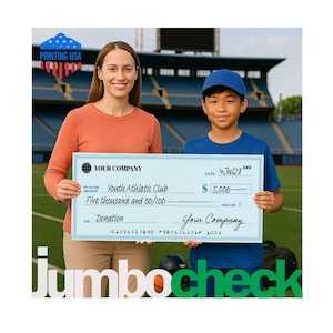 May include: A large, light blue novelty check held by two individuals. The check is printed with 'YOUR COMPANY', 'Youth Athletic Club', 'Five thousand and 00/100', 'Donation', and the date '4Jul28'. It features a dollar sign and the amount $5,000.