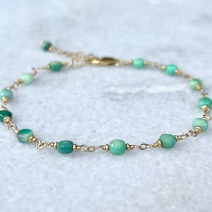 May include: A delicate gold chain bracelet with green gemstone beads. The bracelet is made with small, round beads that are a light green color. The chain is a simple, gold chain.