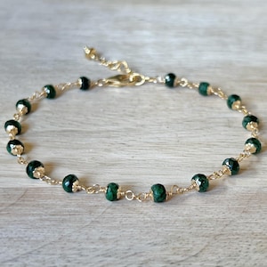 May include: A gold chain bracelet with dark green beads. The bracelet has a clasp closure.