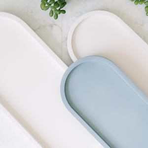 May include: Three oval-shaped trays, one white, one light blue, and one white with a slightly raised edge. The trays are arranged in a stack, with the white tray on top and the light blue tray on the bottom.