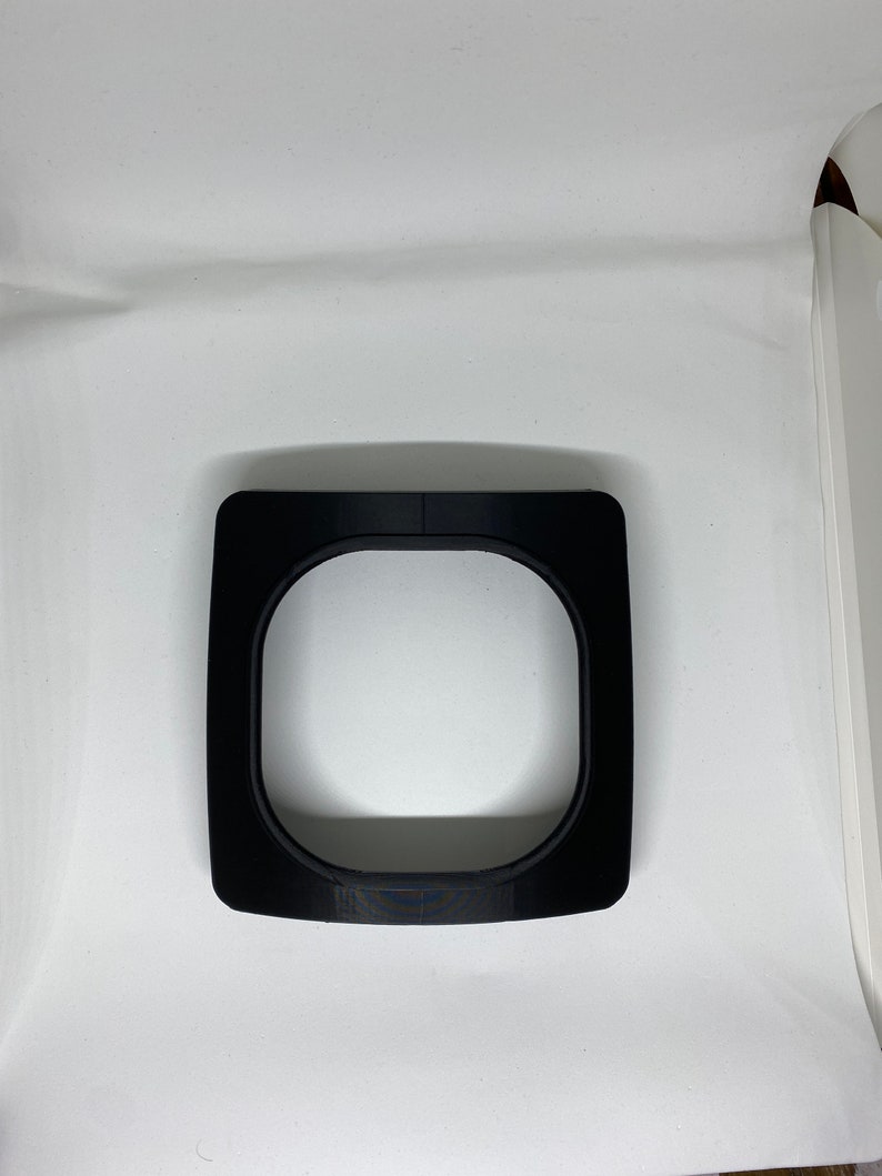 May include: A black plastic ring with a circular opening in the center. The ring is designed to fit around a camera lens.