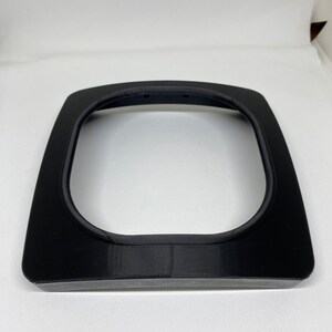 May include: A black plastic frame with a rounded opening, likely for a phone or other device.