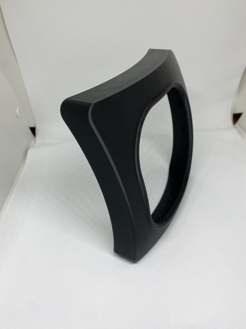 May include: A black plastic curved frame with a circular opening in the center. The frame is designed to hold a round object, such as a clock or a mirror.