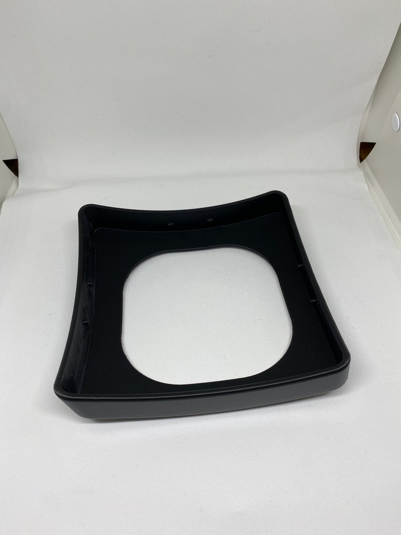 May include: Black plastic base with a circular cutout in the center. The base has a slightly curved shape and is designed to hold a round object.