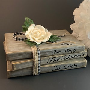 May include: A stack of three wooden boxes with a black and white checkered ribbon and a white flower. The boxes are decorated with the text "Our Story", "The Johnson's", and "Est. 2006".