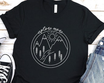 May include: Black t-shirt with a white graphic of mountains, a sun, and trees. The text "explore more" is written above the graphic.