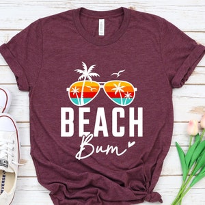 Pode incluir: Camiseta de cor marrom heather com um gr&aacute;fico branco de &oacute;culos de sol com palmeiras refletidas nas lentes. O texto "Beach Bum" est&aacute; abaixo dos &oacute;culos de sol.