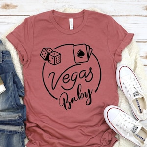 May include: A maroon t-shirt with a black graphic design of dice, playing cards, and the text "Vegas Baby".