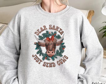 May include: Gray sweatshirt with a Christmas-themed design featuring a cow wearing a red bow in a wreath with the text "Dear Santa Just Send Cows".