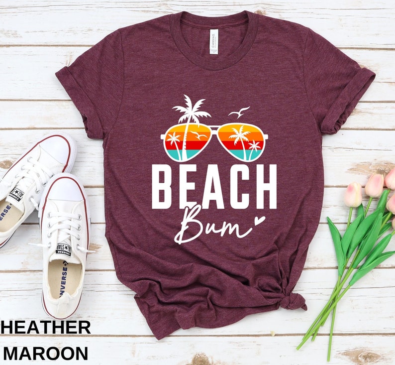 Pode incluir: Camiseta de cor marrom heather com um gr&aacute;fico branco de &oacute;culos de sol com palmeiras refletidas nas lentes. O texto "Beach Bum" est&aacute; abaixo dos &oacute;culos de sol.